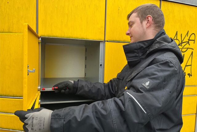 Mitarbeiter der DHL Group verschraubt die Tür einer Packstation.