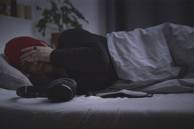 Eine Frau liegt im abgedunkelten Zimmer auf dem Bett, neben ihr ein Gehörschutz.
