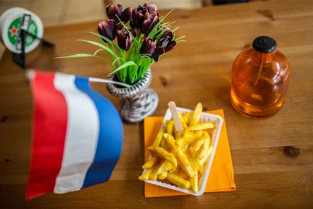 Eine Schale Pommes steht auf einem Tisch, der mit Tulpen und einer niederländischen Flagge dekoriert ist.