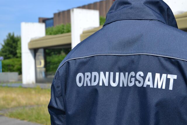 Ein Mitarbeiter des Ordnungsamtes steht mit dem Rücken zur Kamera vor dem Rathaus in Castrop-Rauxel. Auf seiner Jacke ist der Schriftzug „Ordnungsamt“ zu lesen.