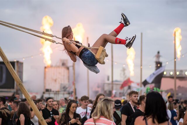 Eine Frau schaukelt auf dem Musikfestival Parookaville in Weeze (NRW). Unter ihr stehen feiernde Festivalbesucher.