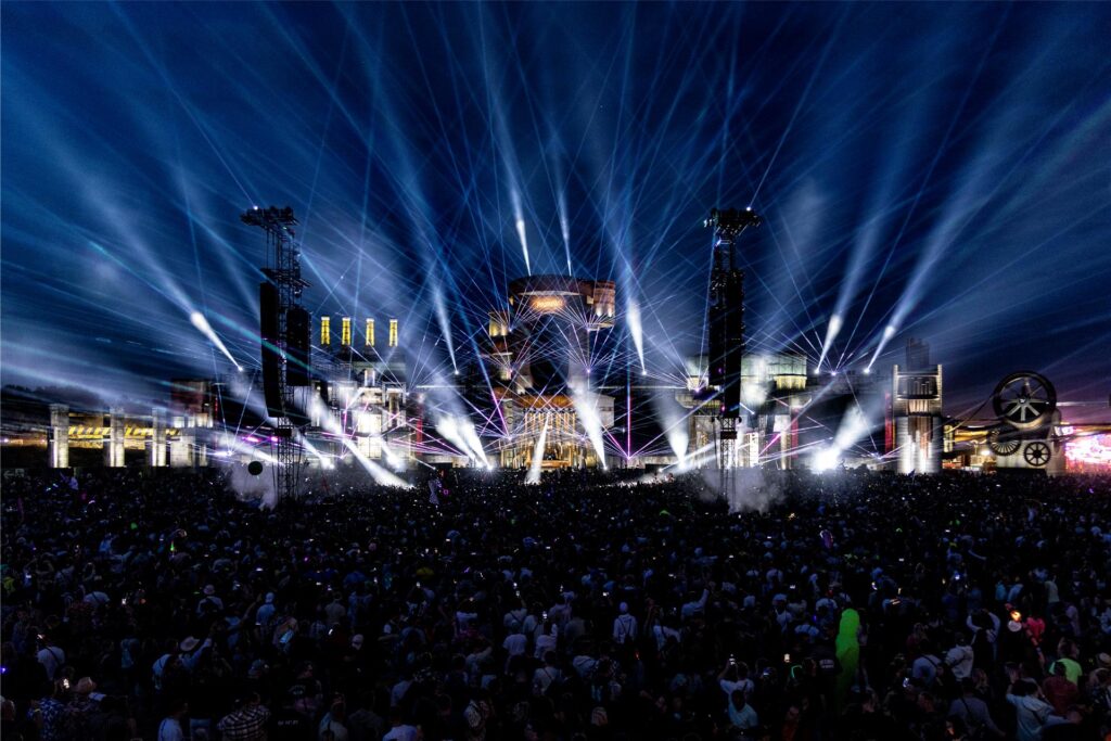 Feiernde Menschen stehen vor der Hauptbühne beim Parookaville. Der Himmel ist von der Lasershow hell erleuchtet.