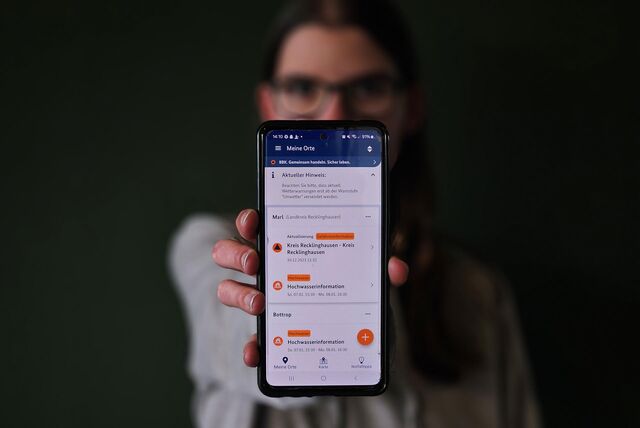 Katharina Göke hält ein Handy, das die Warn-App NINA zeigt, in die Kamera.