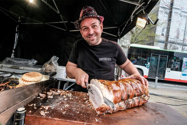 Ein Mann mit Hut schneidet einen Schinken in einem Foodtruck.