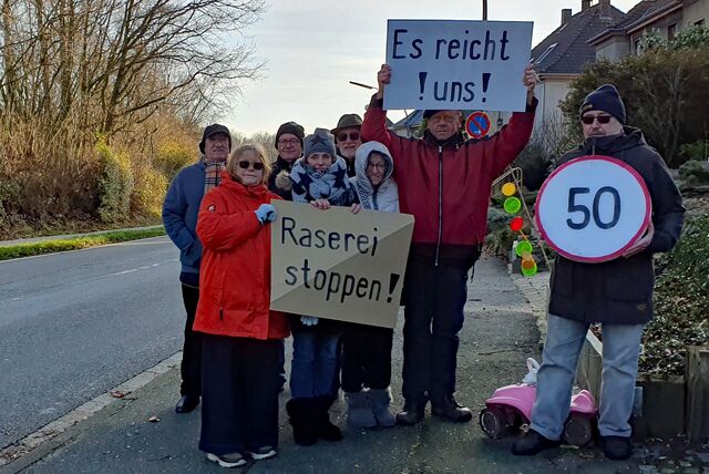 Eine Gruppe Menschen hält an der Holtgarde Schilder hoch, die darauf hinweisen, dass hier nicht mehr gerast werden soll.