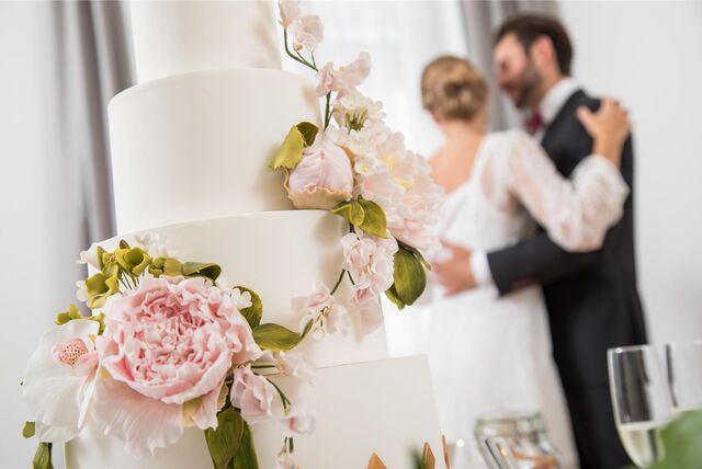 Ein Brautpaar tanzt neben einer weißen Hochzeitstorte.