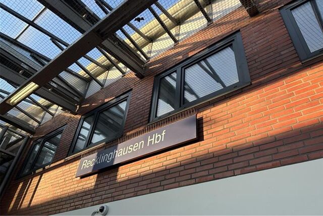 Bahnhofsschild vom Recklinghäuser Hauptbahnhof vor einer Ziegelwand.