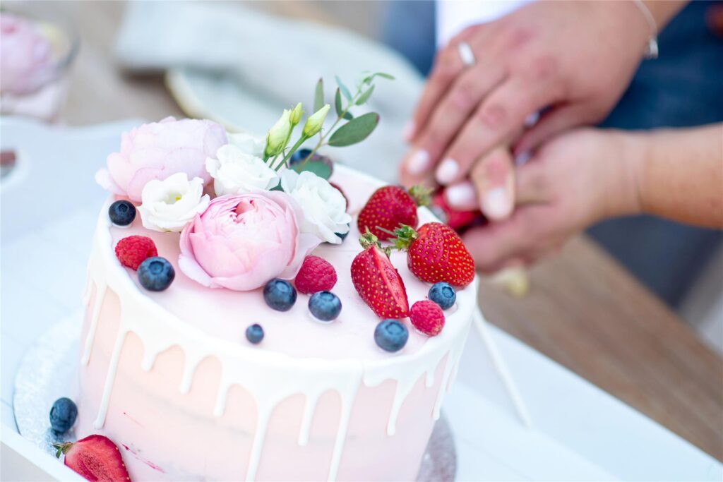 Eine mit Früchten und Blumen dekorierte Hochzeitstorte wird angeschnitten. 
