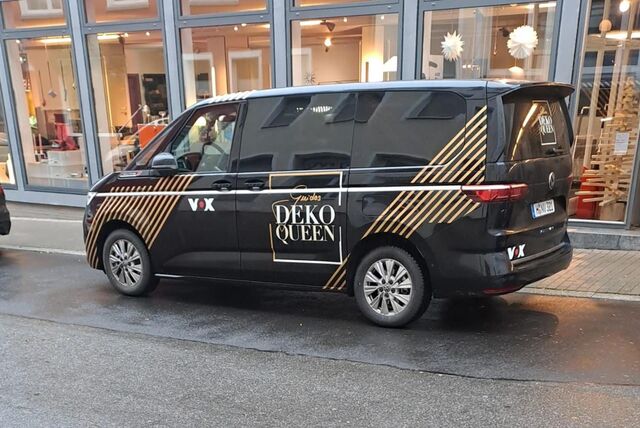 Ein schwarzer Bulli steht am Straßenrand. Eine Aufschrift auf dem Wagen zeigt, dass es sich um den Wagen von der Sendung „Deko Queen“ handelt.