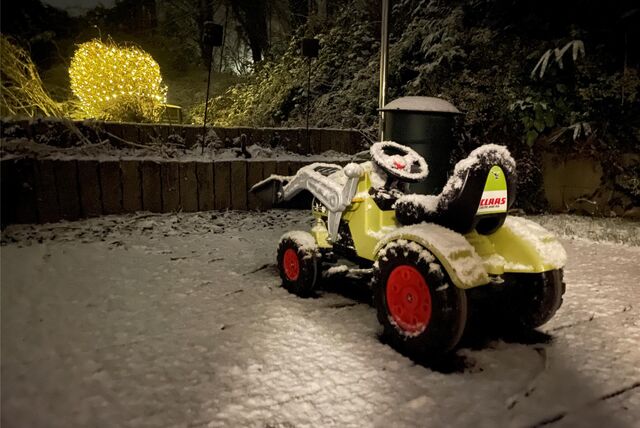 Schnee liegt auf einem Spielzeug-Traktor im Garten und auf einer Terrasse.