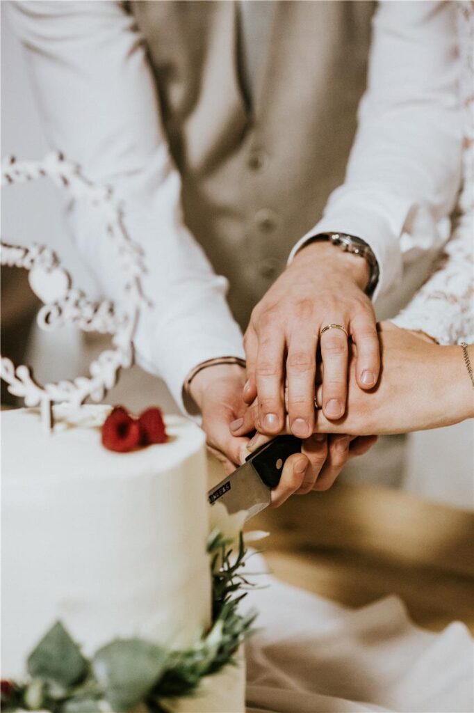 Nahaufnahme von den Händen eines Brautpaares, das die Hochzeitstorte anschneidet.