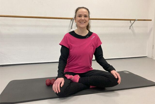 Ursula Jostes aus Waltrop sitzt in Sportkleidung im Schneidersitz auf einer Übungsmatte in der Tanzschule Tanzhof an der Hilberstraße in Waltrop. Im Hintergrund ist vor der weißen Wand eine Ballettstange zu sehen.