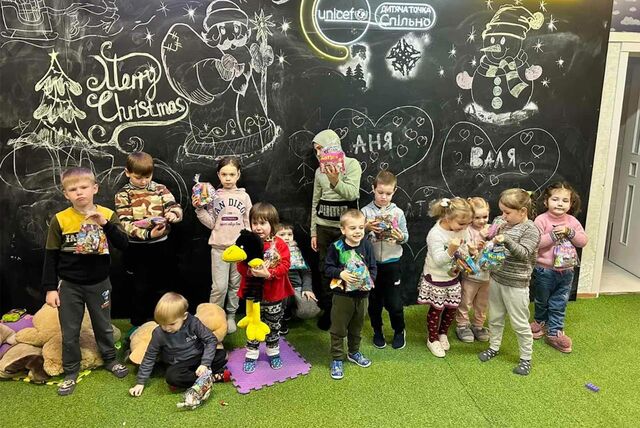 13 Kinder stehen nebeneinander und packen Geschenktüten mit Süßigkeiten aus.