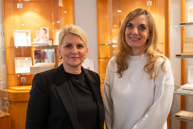 Zwei Frauen stehen vor Ausstellungsvitrinen eines Juweliers und schauen in die Kamera.