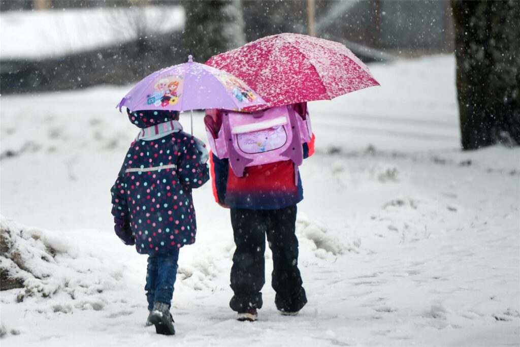Zwei Kinder gehen mit Regenschirmen durch Schneefall.