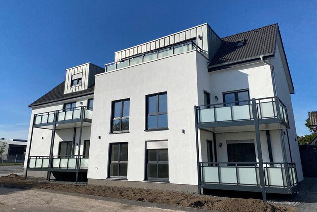 Ein Neubau bzw. Mehrparteienhaus mit hohen Fenstern, vier Balkons und einer Dachterasse