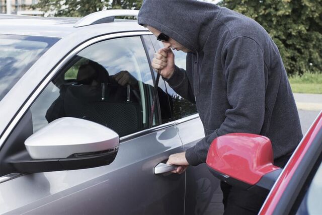 Ein junger Mann im Kapuzenpulli bricht ein Auto auf.
