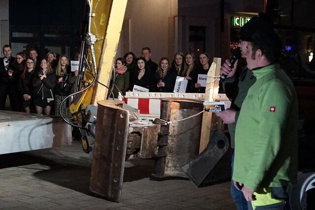 Mehrere junge Männer und Frauen in festlicher Kleidung stehen in der Dunkelheit in Waltrop vor der Stadthalle neben einem Bagger, dessen Schaufel auf dem Pflaster des Vorplatzes liegt.