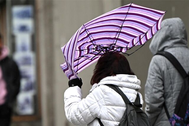 Eine Passantin mit wehenden Haaren sichert bei einem Sturm ihren Regenschirm