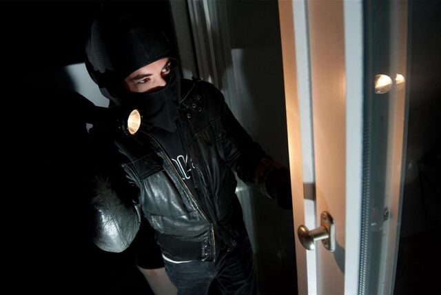 Ein Mann mit Maske und Taschenlampe steht vor einer Tür (Symbolbild)
