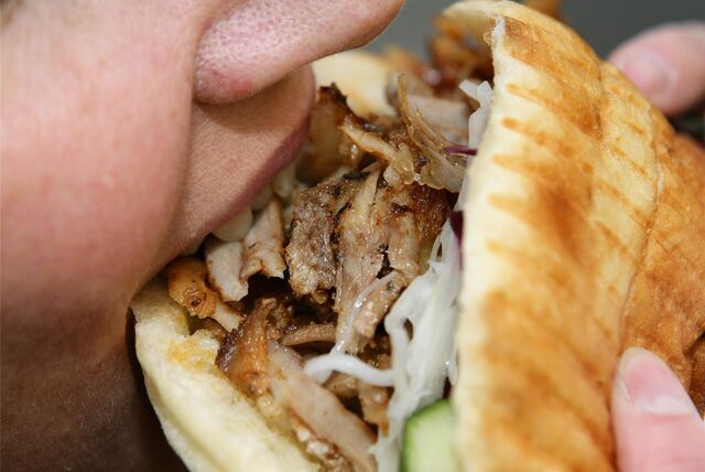 Eine Person beißt in eine mit Fleisch und Salat gefüllte Dönertasche.