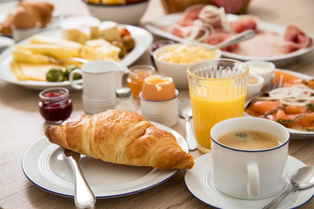Ein üppiges Frühstück mit Croissant, Kaffee, Orangensaft und Aufschnitt steht auf einem Tisch.