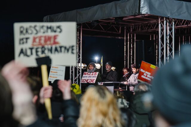 Ein Blick durch die Menschenmenge bei der Kundgebung „Laut sein – jetzt! Gemeinsam gegen Rechts“ am Europaplatz in Castrop-Rauxel auf die Bühne. Viele Menschen halten Schilder in die Höhe. Auf einem steht beispielsweise: Rassismus ist keine Alternative.