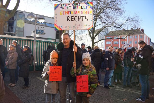 Ein Mann und zwei Mädchen stehen nebeneinander auf einer Kundgebung gegen Rechts.