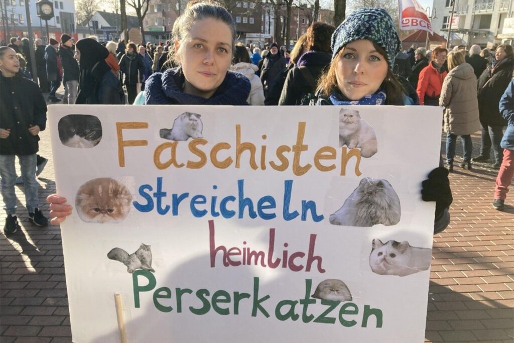 Zwei Frauen halten ein Plakat in die Höhe. Darauf steht Zwei Frauen halten ein Plakat in die Höhe. Darauf steht