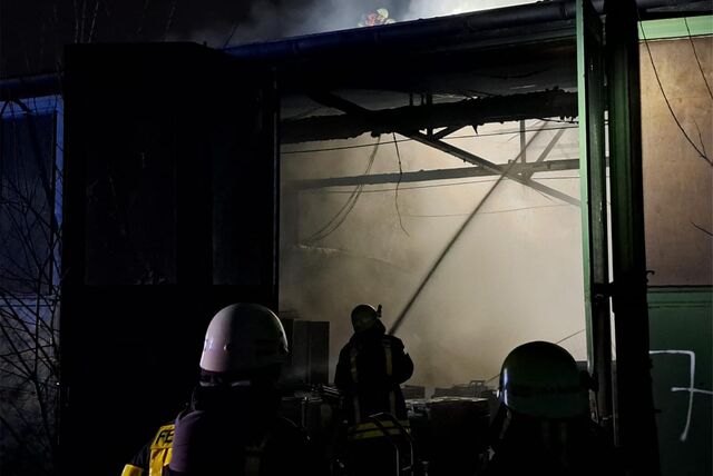 Feuerwehrleute löschen einen Brand in einer verrauchten Lagerhalle.