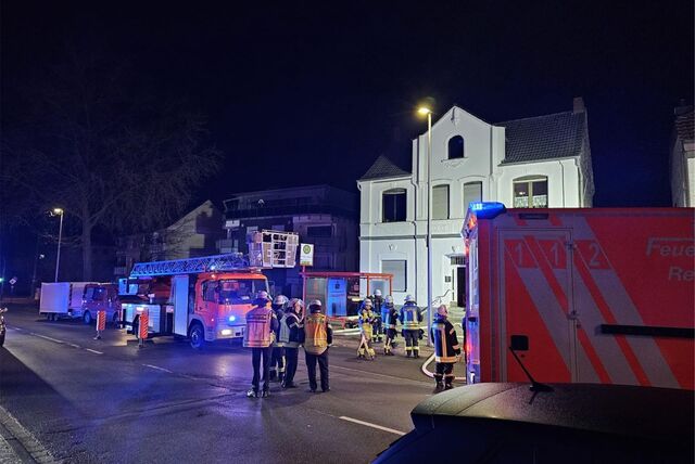 Feuerwehrleute stehen vor einem brennenden Haus.