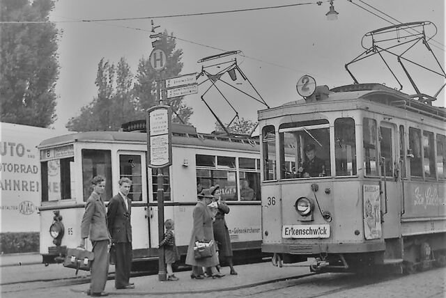 Menschen stehen vor zwei Straßenbahnen und warten.