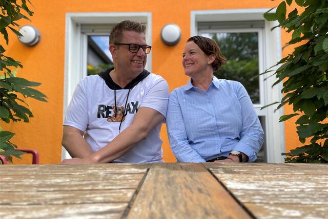 Jörg Schlösser und Susanne Rosenberger sitzen an einem Tisch vor dem Sitz der „Pflegedienst & Tagespflege S. Rosenberger GmbH“.