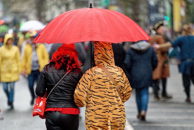 Verkleidete Karnevalisten unterwegs mit Regenschirm.