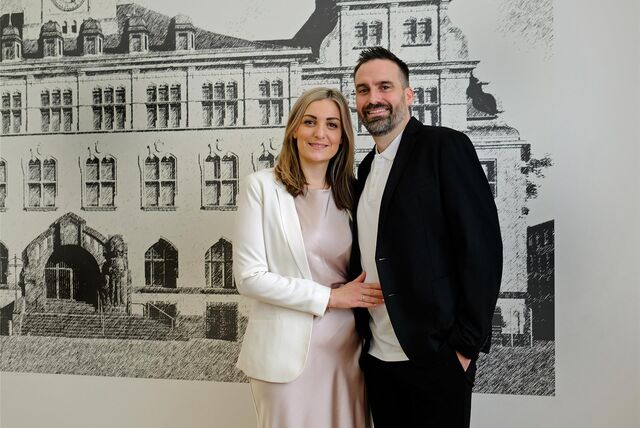 Stefanie Bumbic und Jesper Holtkamp stehen vor einem Foto des Recklinghäuser Rathauses.