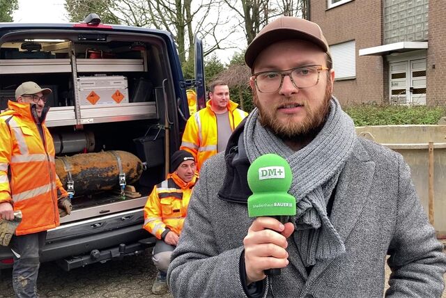 Ein Mann mit Mikrofon steht vor einem Transporter, auf dem der Blindgänger aufgeladen wurde.