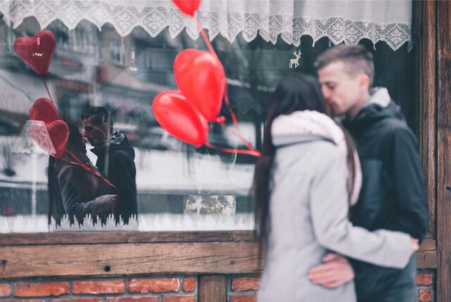 Ein Mann und eine Frau umarmen sich und halten Herzluftballons in der Hand.