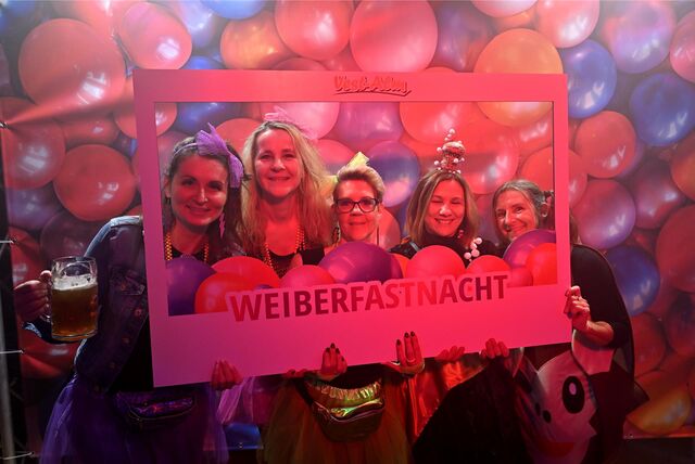 Kostümierte Frauen halten einen Rahmen mit der Aufschrift „Weiberfastnacht“.