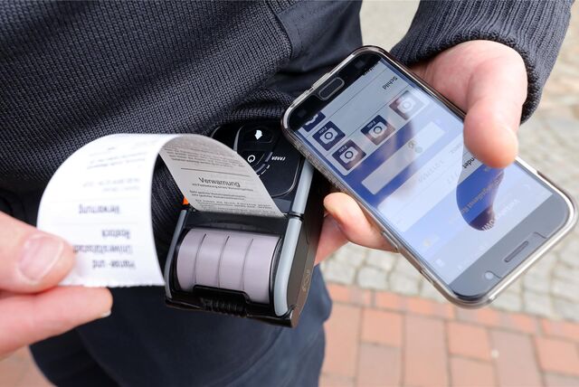 Eine Politesse steht neben mehreren geparkten Autos und stellt einen Strafzettel aus.