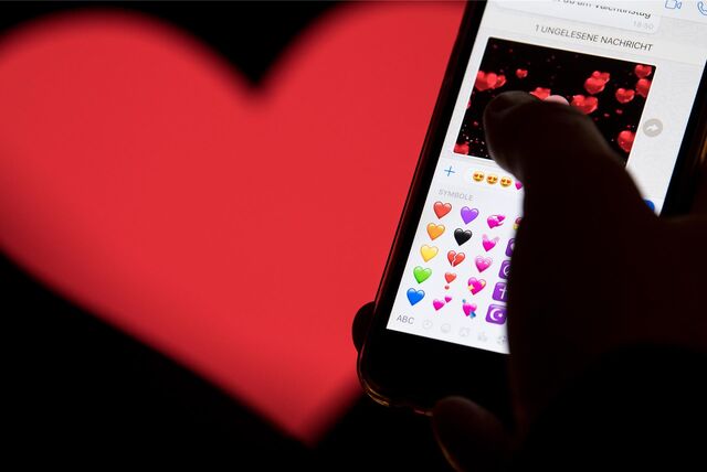 Eine Hand tippt eine Liebes-Nachricht in ein Smartphone, im Hintergrund ist ein großes Herz zu sehen.