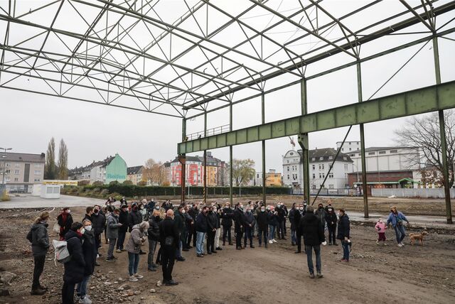 Menschen stehen unter dem Skelett einer früheren Stahlhalle.