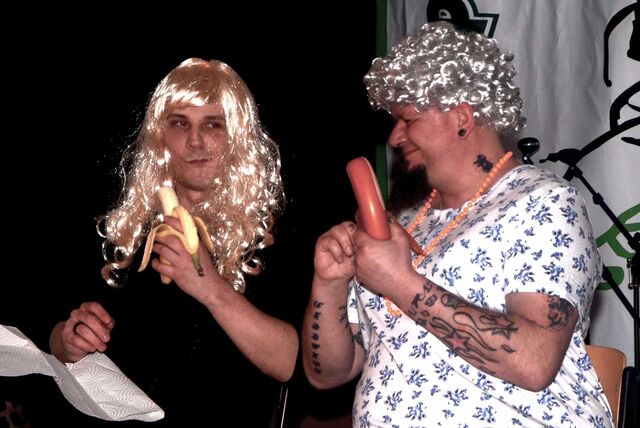 Zwei als Frauen kostümierte Männer essen während einer karnevalistischen Shownummer auf einer Bühne in Waltrop eine Banane und eine Fleischwurst.