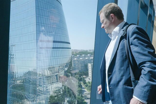 Der Politiker Frank Schwabe steht in einem Gebäude an einem großen Fenster und blickt auf ein Hochhaus mit gläserner Fassade.