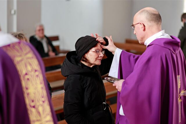Ein Pfarrer zeichnet einer Frau am Aschermittwoch ein Aschenkreuz auf die Stirn.