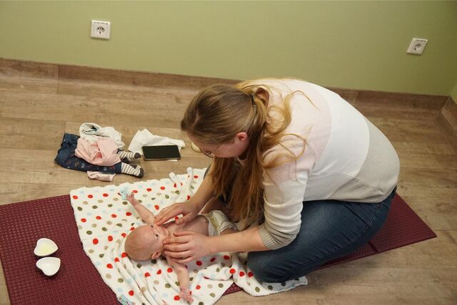 Eine Mutter und ihr Baby knien auf einer bunten Matte. Das Baby wird massiert.