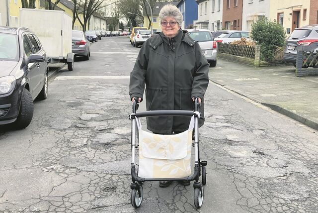 Eine Frau mit Rollator auf einer Straße mit zahllosen Schlaglöchern.
