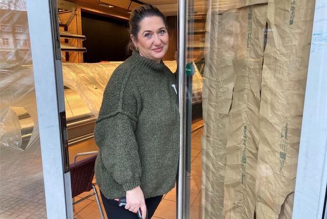 Aida Suvalic öffnet die Tür eines Cafés, die mit Folien und Papier abgeklebt ist. Im Hintergrund ist eine Theke zu sehen, die ebenfalls von einer Folie vor Schmutz geschützt wird.