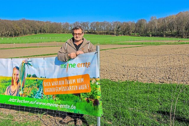 Bauer vor einem großen Acker, die Sonne scheint, der Himmel ist blau. Vor ihm ein Werbeplakat.