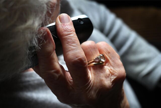 Das Foto zeigt eine Seniorin von hinten, die einen Telefonhörer in der rechten Hand hält.