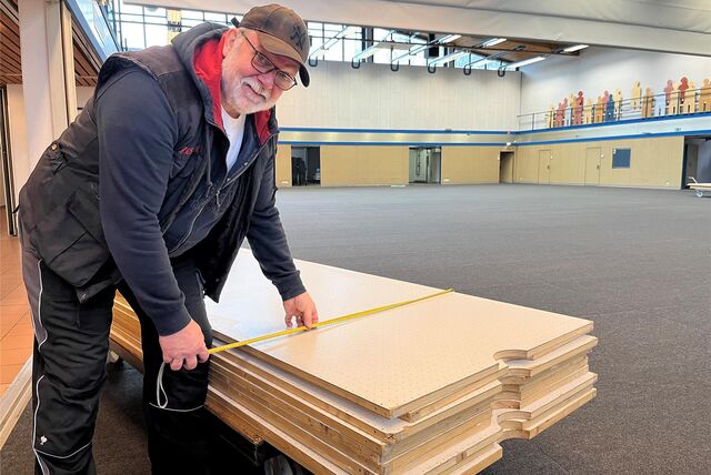 Ein Mann in Arbeitskleidung misst in der Seestadthalle Holzpaneelen ab.